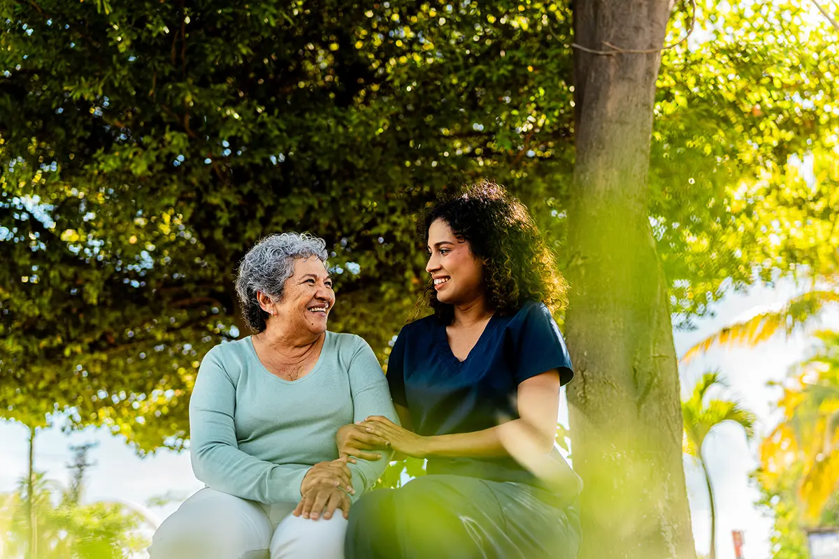 A senior adult sits under a tree with their daughter